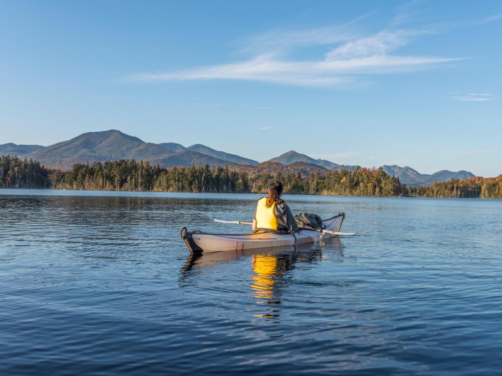 Woman kayaks within a white kayak in a remote lake called Boareas Ponds in the Adirondacks with the mountains in view