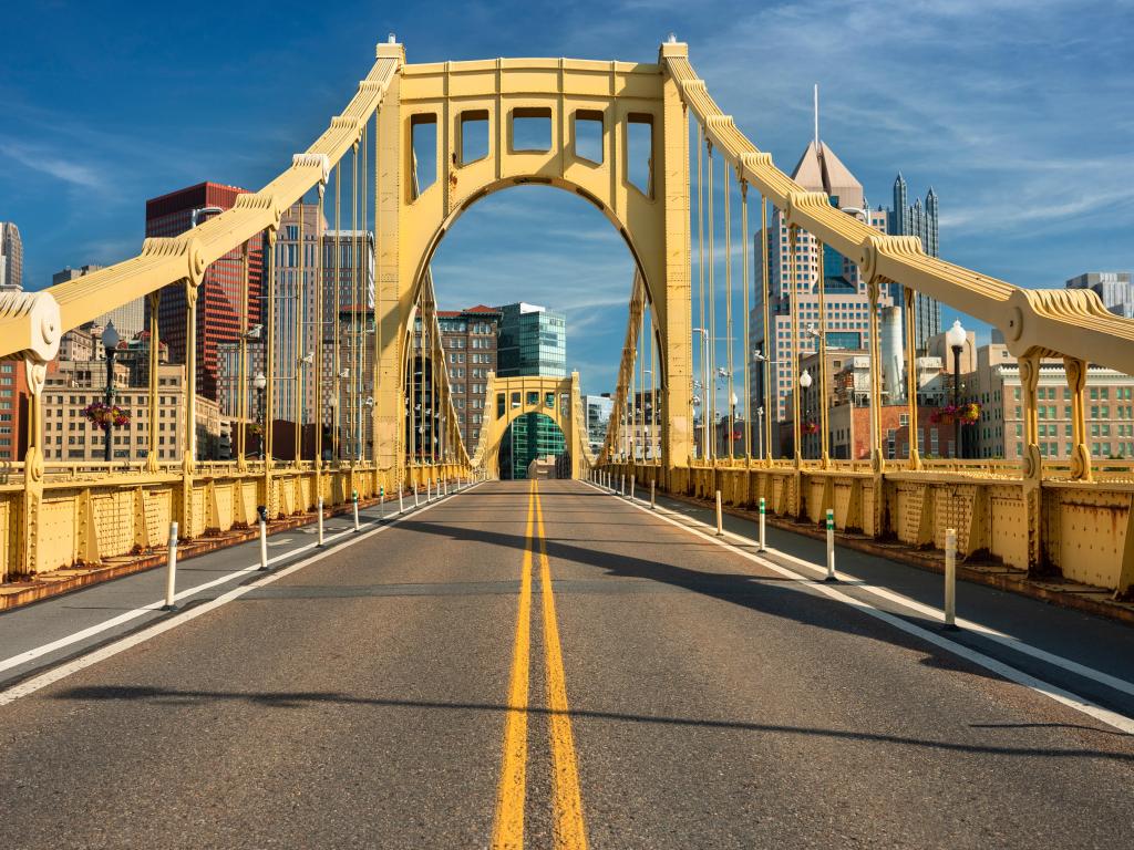 Traffic and people cross the Allegheny River on the steel Roberto Clemente Bridge in downtown Pittsburgh, with blue sky above