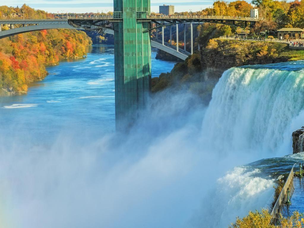 Large waterfall with bridge crossing wide river to one side