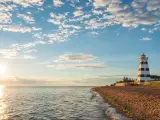 West Point Lighthouse at Cedar Dunes Provincial Park, Prince Edward Island, Canada take just before sunset with a blue sky and a scattering of cloud and the sea against the sandy shore. 