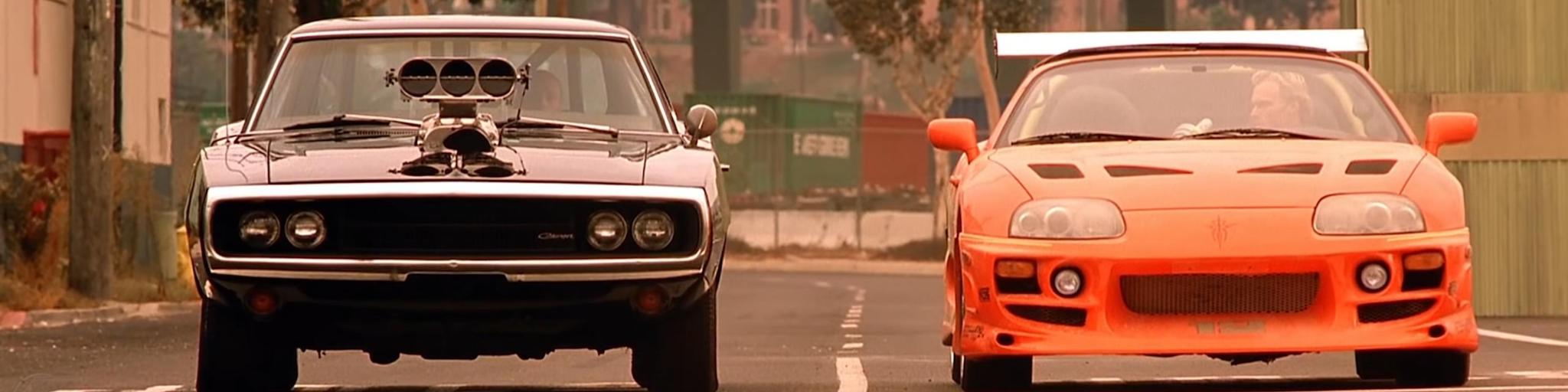 Two cars, one black and one orange, with the main characters of the Fast and Furious movie, Dom and Brian, about to start a race.