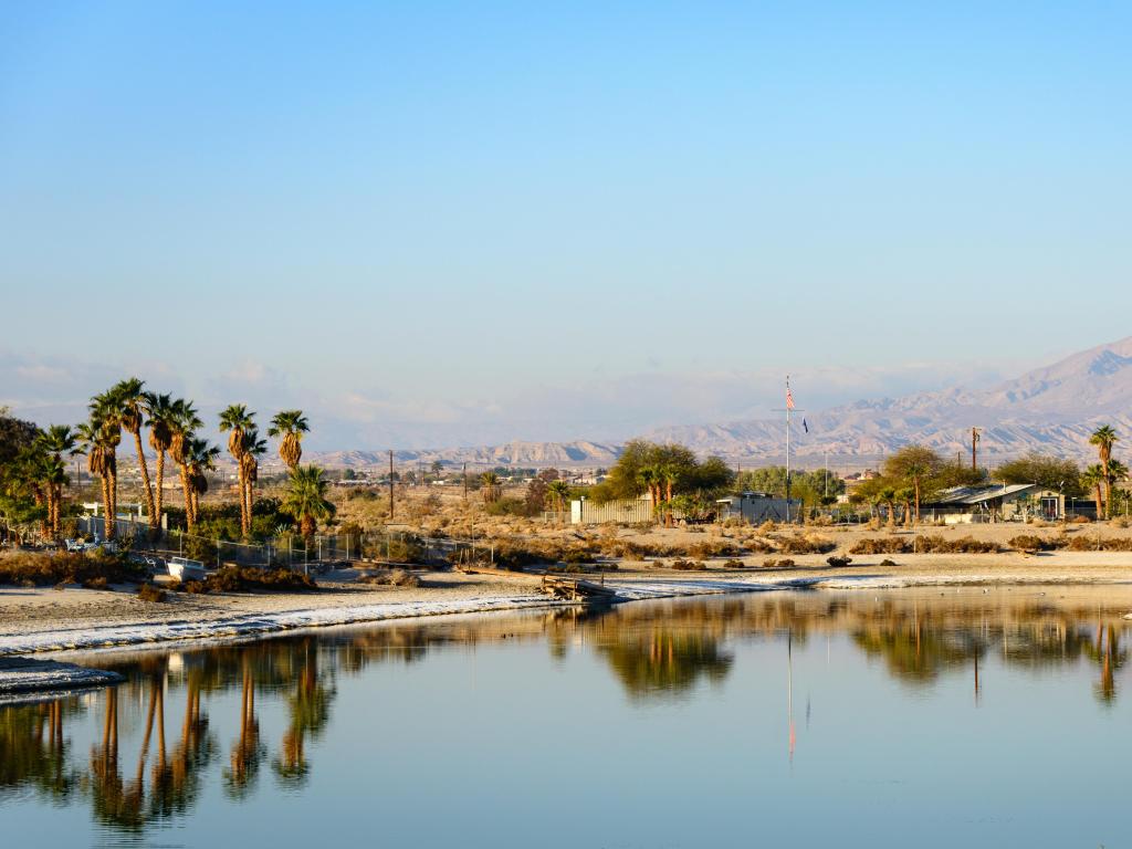 Salton Sea, California, USA with the lake in the foreground, palm trees and mountains in the distance on a foggy but sunny day.