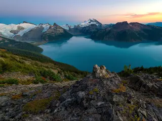 Garibaldi Provincial Park, Canada taken at sunset with a rocky landscape in the foreground, a lake and mountains in the distance. 