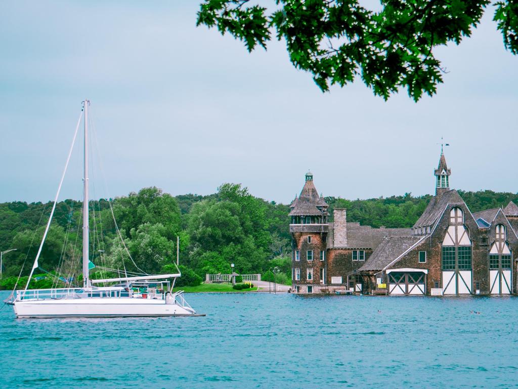An impressive boat house in the background, and sailboat passing through Lake Ontario, New York