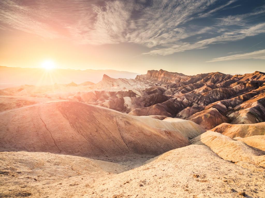 Death Valley, California, USA with a red sunset at Zabriskie Point in Death Valley, California with sun in the frame and orange flare, blue sky and vibrant rock ridges.