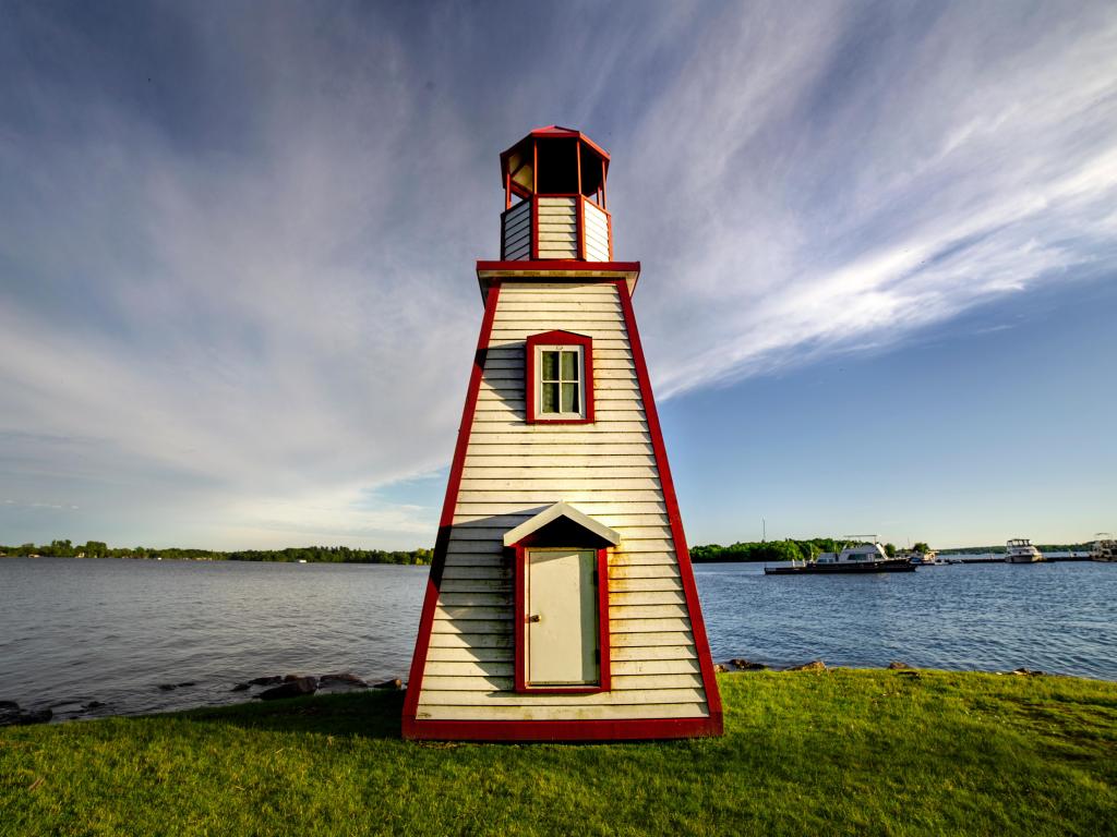 Red and white wood built lighthouse overlooking wide river with cloudy sky and boat