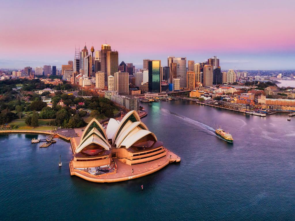 Pinkish colourful sunrise over Sydney city CBD on waterfront of Harbour around Circular quay with major architectural landmarks and symbols of Australia.