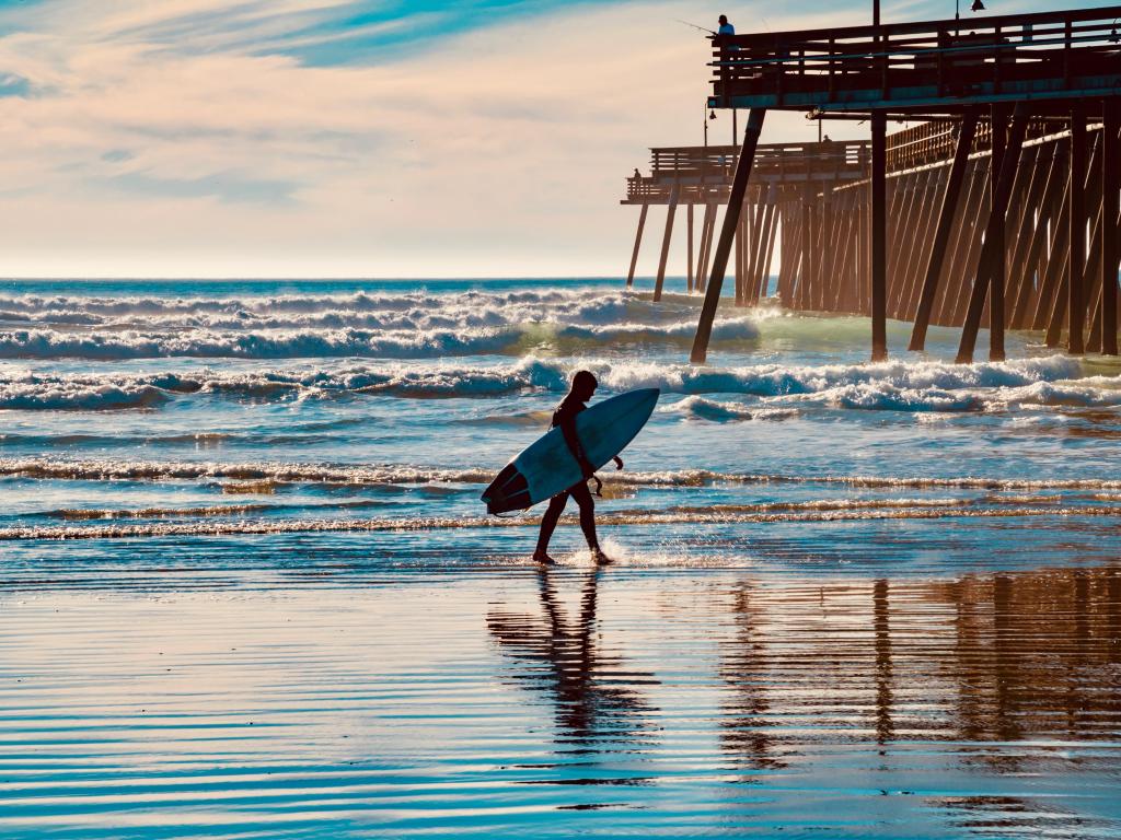 Young man with a surfboard on the California beach in the town of Pismo Beach