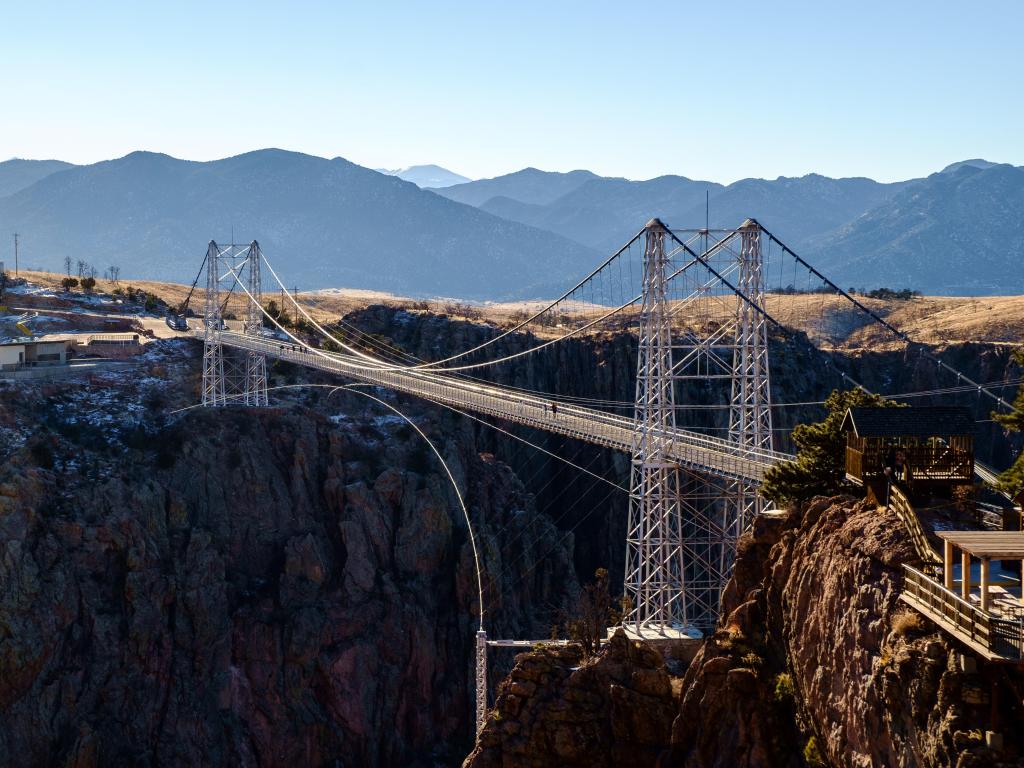 A view of the suspension bridge from a vantage point with mountains and blue sky in the background
