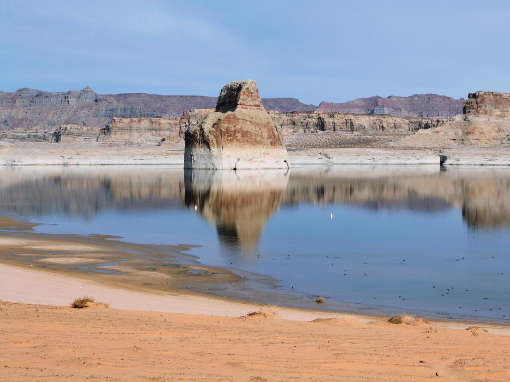Lone Rock in Lake Powell, Arizona, USA with the lake in the foreground and a blue sky.
