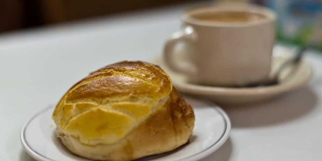 A bread roll, known as a Pineapple bun in front of a cup of tea, on a white table