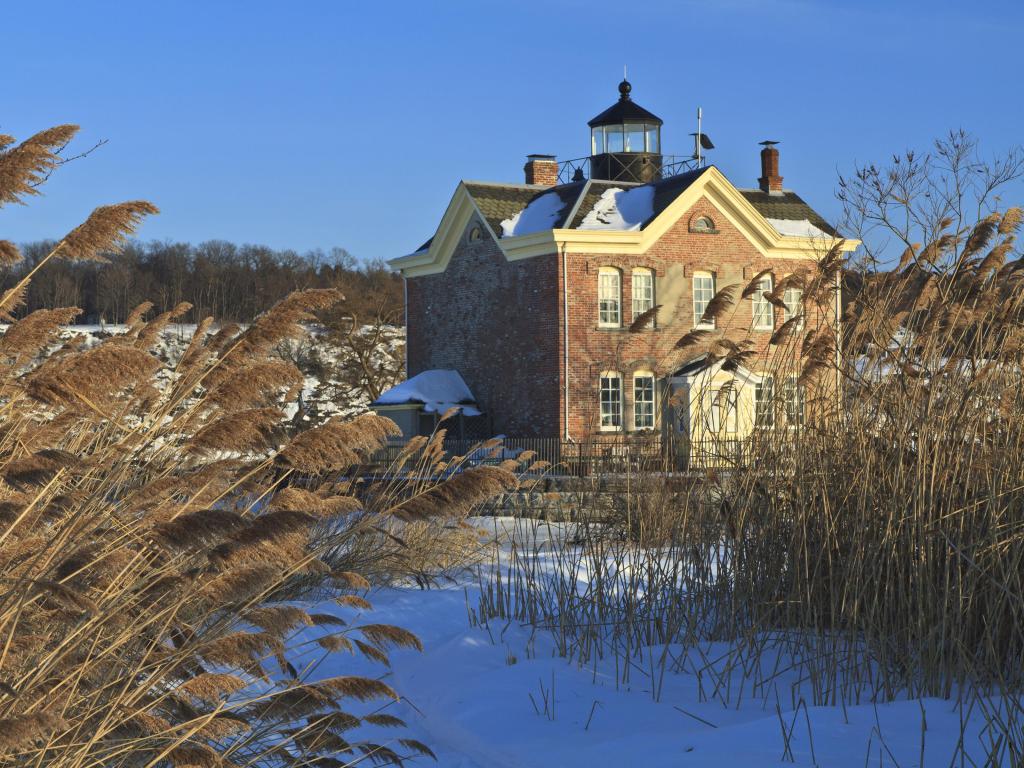 Windswept sea oats front the snow clad Saugerties Lighthouse on a sunny, cold day