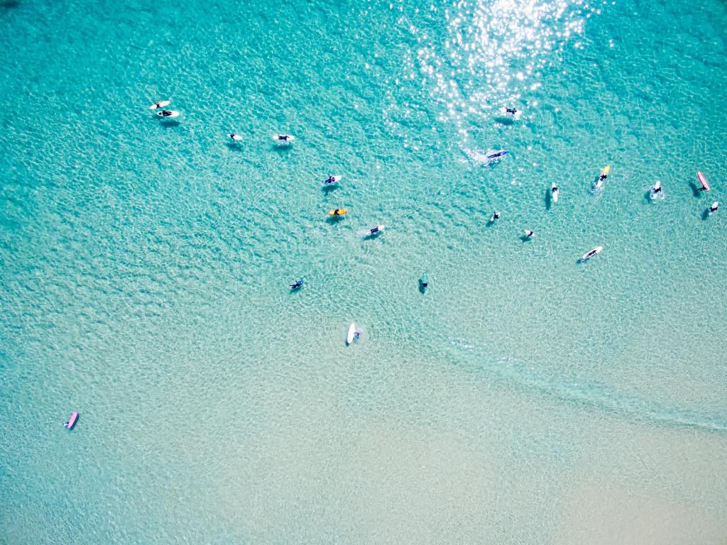 An aerial view of surfers taken from high above on turquoise water in bright sunshine