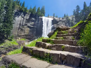 Stepping leading up Mist Trail, with waterfall in the background, surrounded by pine forests