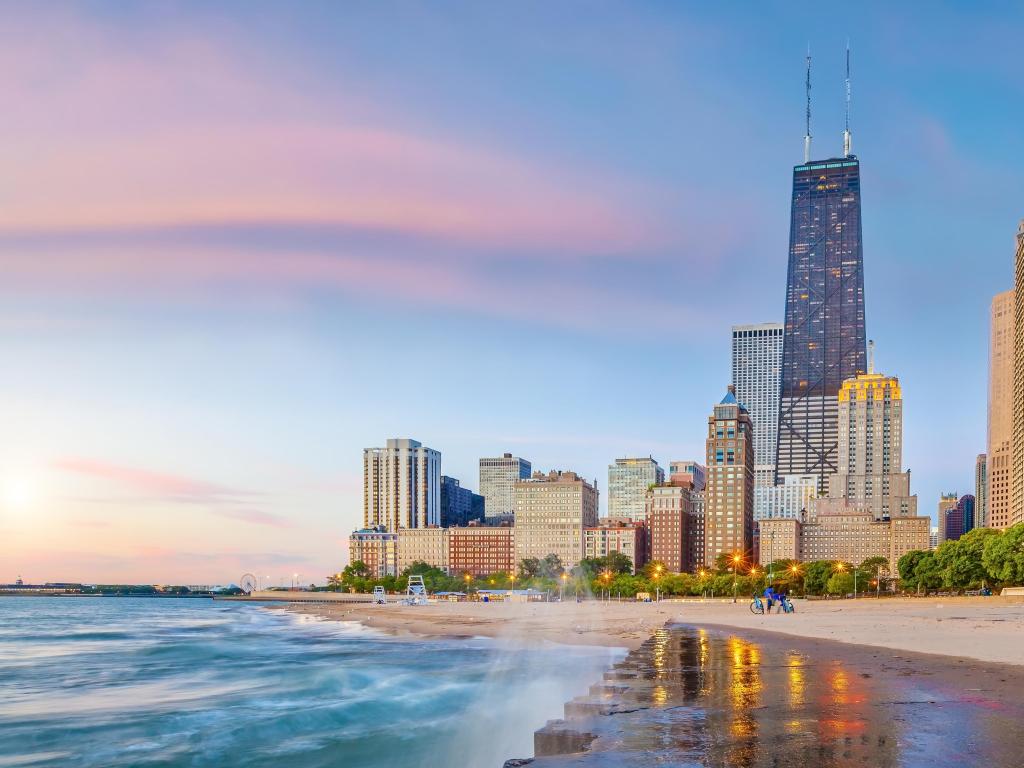 Chicago, Illinois, USA with the downtown city skyline the background at sunset and the shore of Lake Michigan in the foreground.