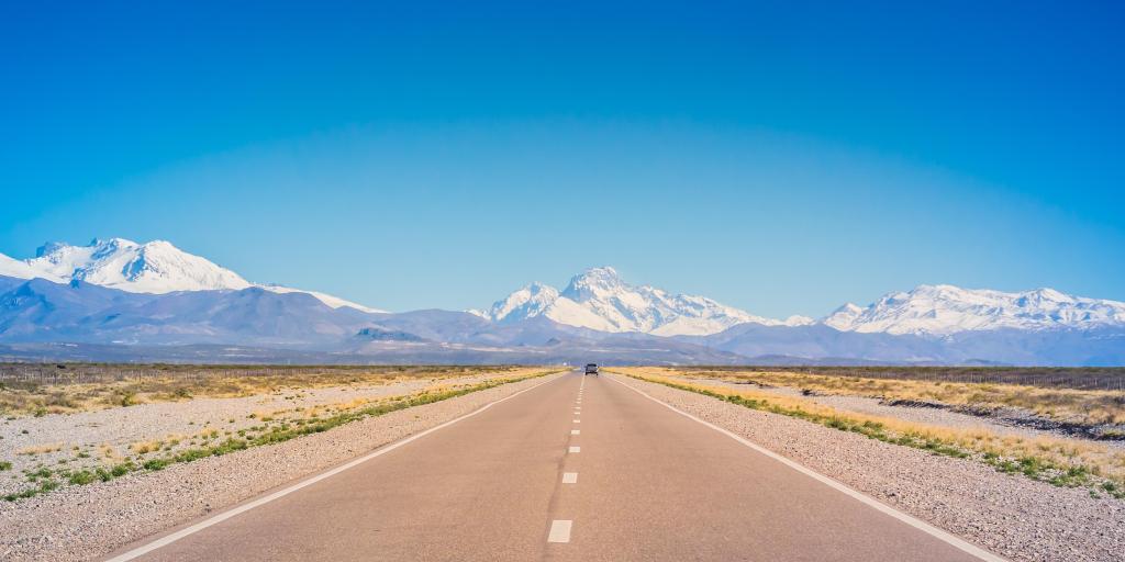A car on an empty road in Mendoza, Argentina, with mountains in the background