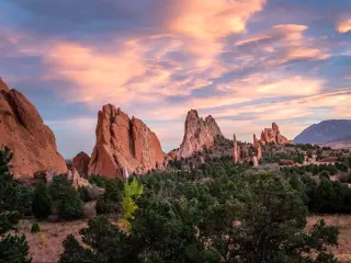 Garden of the Gods, Colorado Springs at sunset with green trees in the foreground and the jagged rock formations in the background.
