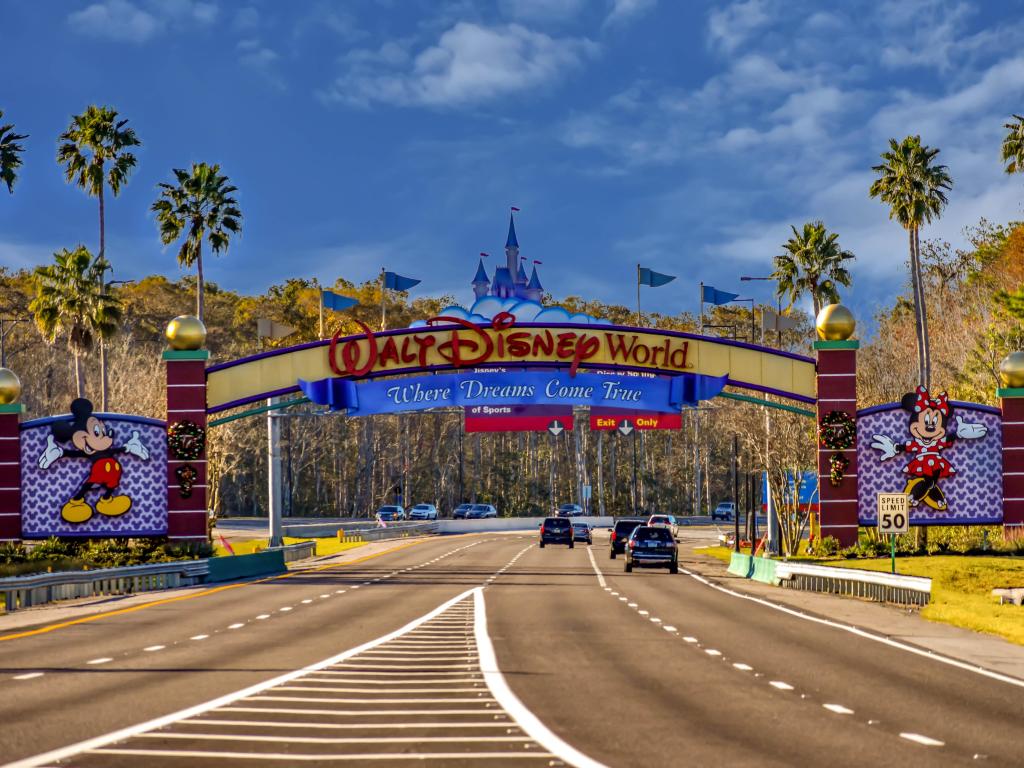 Cars driving on a road under the Walt Disney World Entrance Arch in Orlando Florida, with a blue sky above.