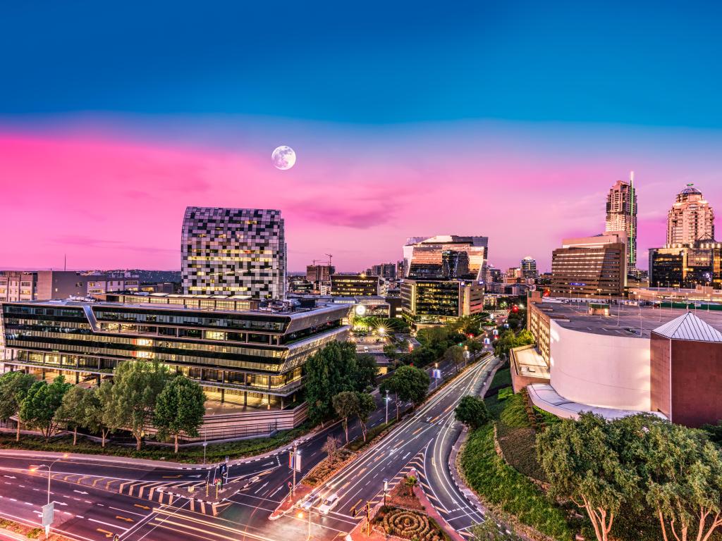 The skyline of Sandton district of the city with a pink sunset, full moon in the background