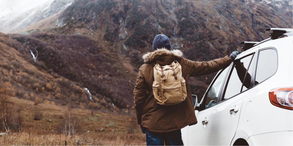 A man standing with his car with mountains in the distance 