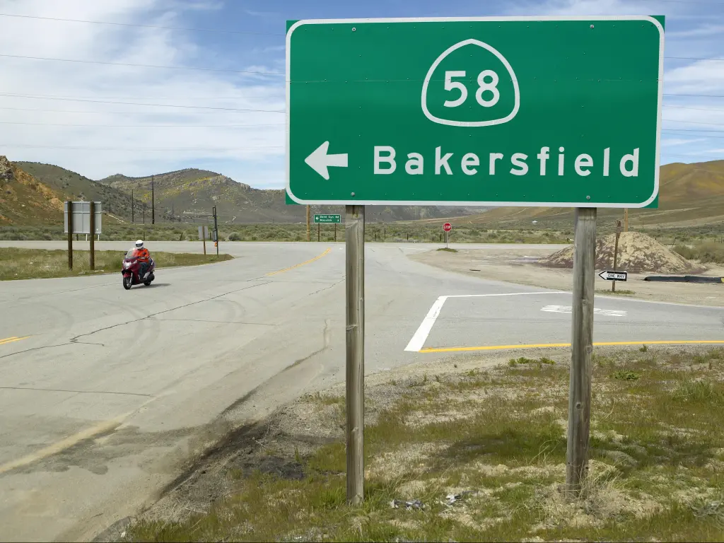 Motorcycle driving past a green road sign that says "58" with an arrow pointing left to Bakersfield 