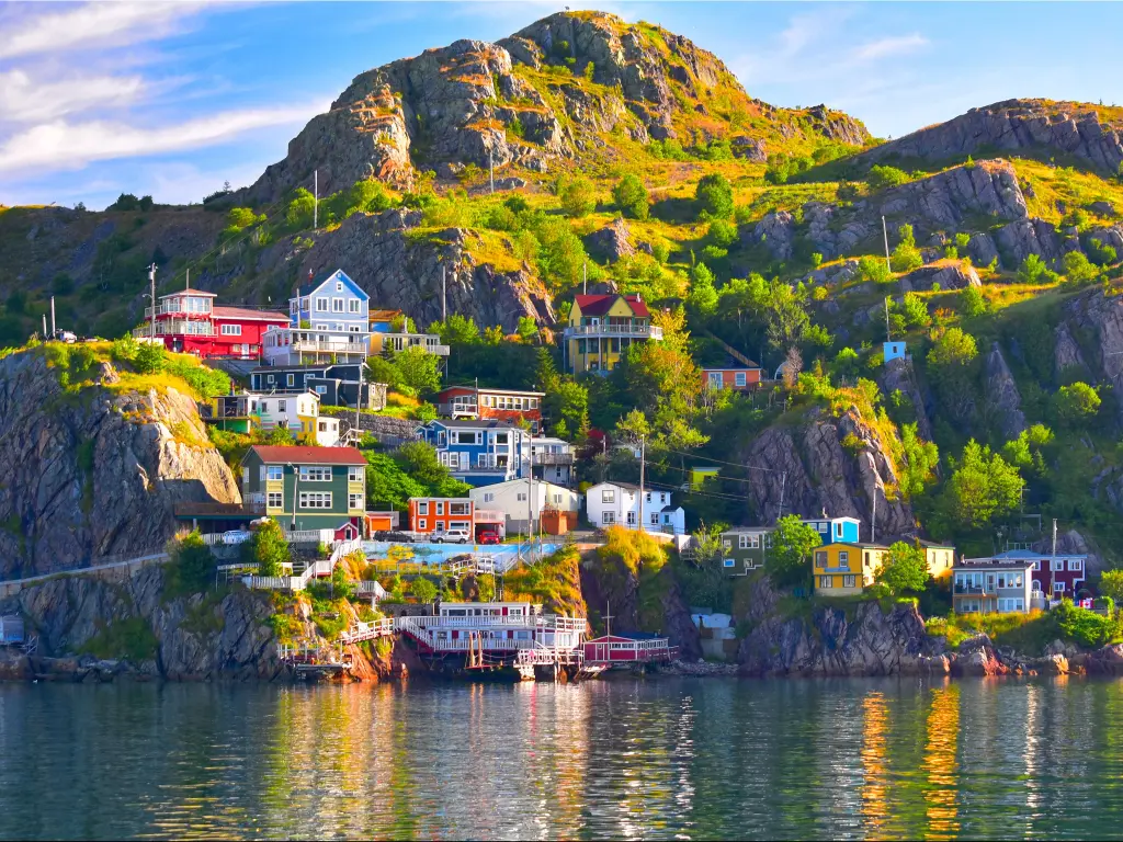 St John's harbour, Newfoundland, Canada with the sea in the foreground looking at the a community of beautifully coloured buildings on the island which is steep with rocks and large green areas on a sunny day. 