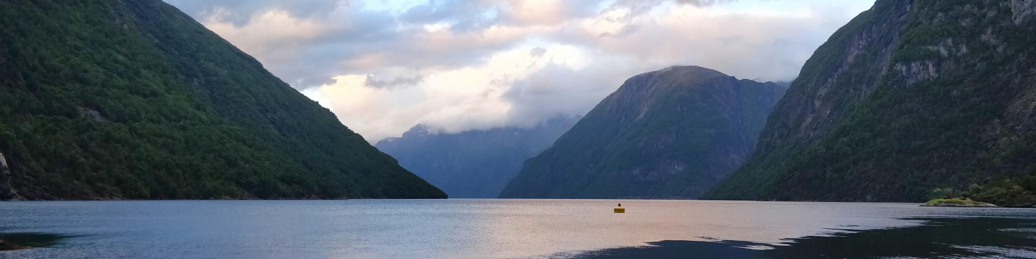Clouds and mountains reflect in the fjord's water in Hellesylt, Norway