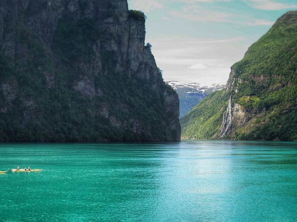 Kayakers row in the turquoise Norwegian fjord, with the Seven Sisters waterfalls in the distance