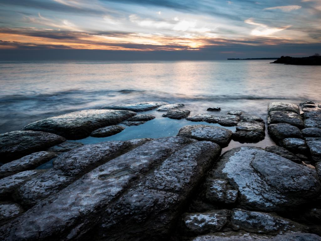 Rocks on the shore at Lake Ontario at Cobourg, Canada at sunset, with the lake shimmering in the evening light