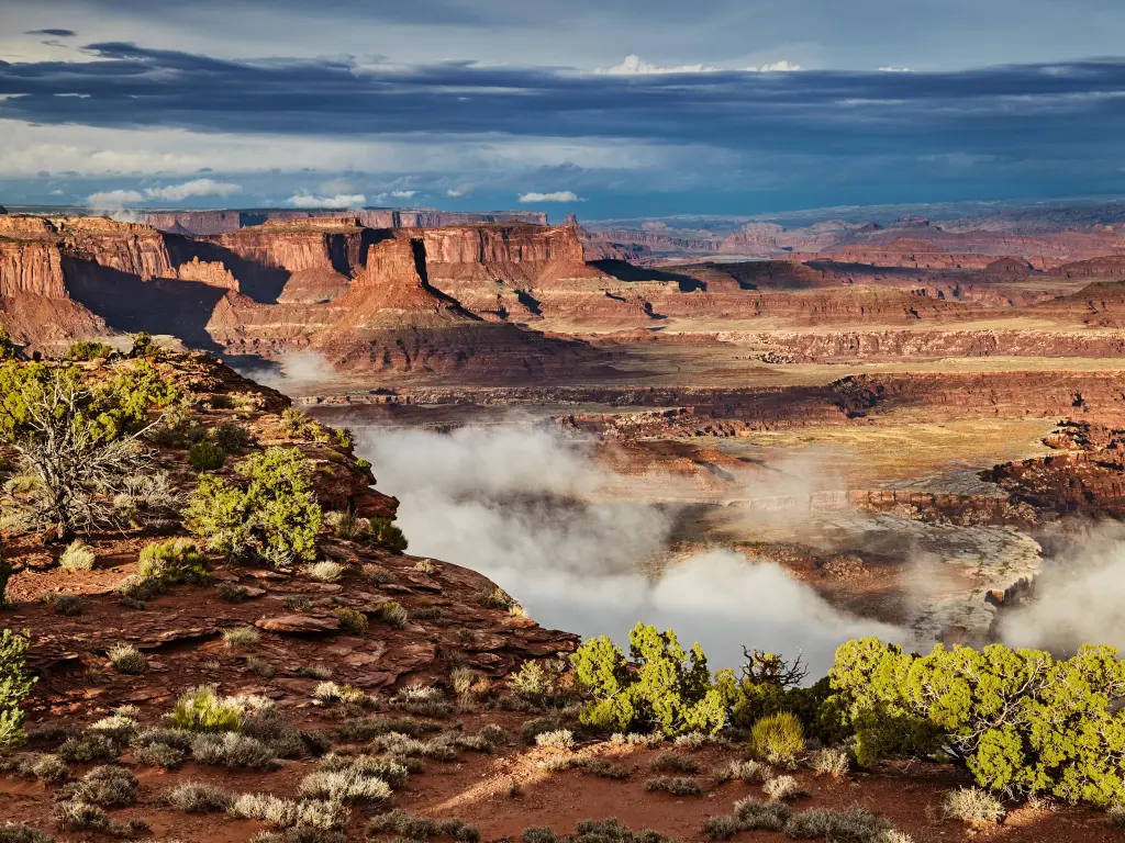 Mist rolls in over the red rocks at Island in the Sky, Canyonlands, Utah, with a foreboding gray sky hanging over above