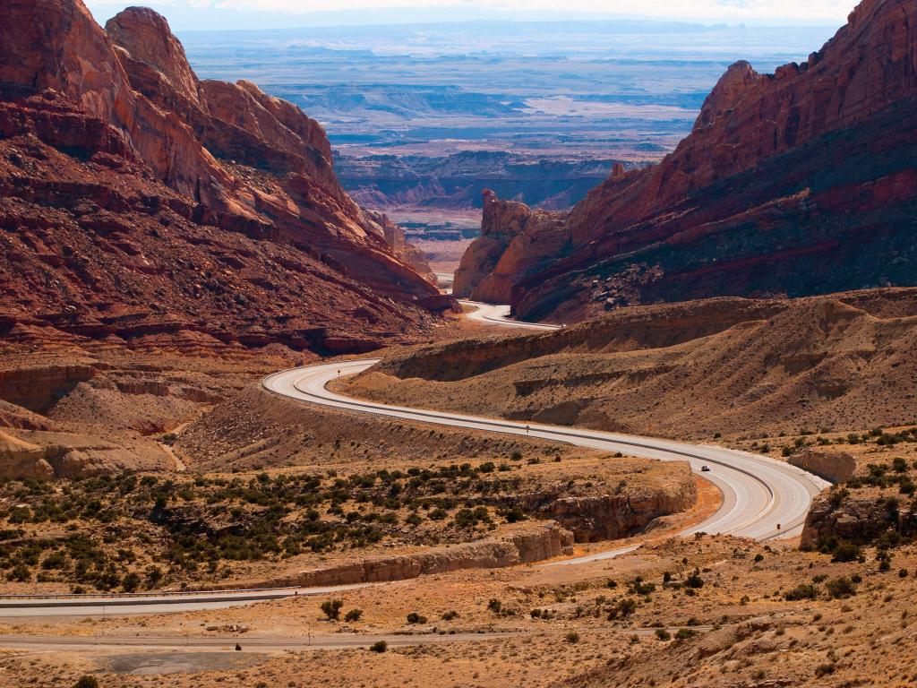 Winding road cutting between orange rocks looking out onto wide dry landscape