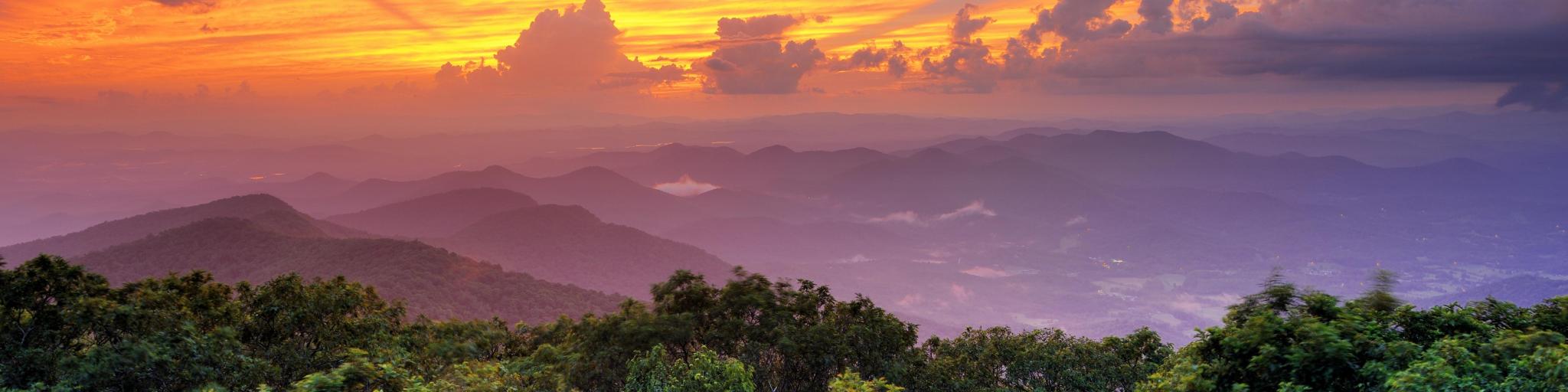 Georgia's Blue Ridge Mountains at sunset with trees in the foreground and an orange and purple sky above