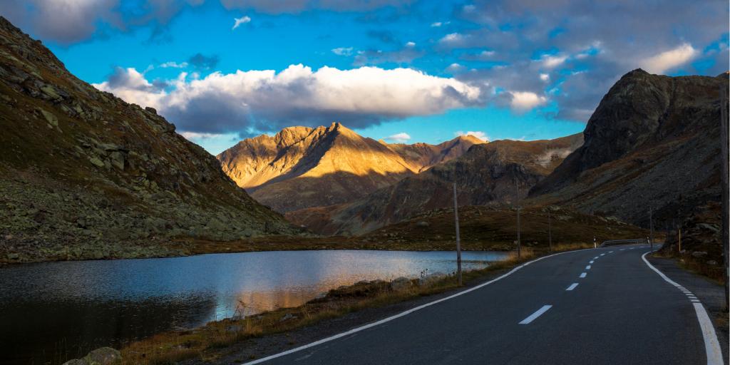 The Flüela Pass in Switzerland skirts by a lake between mountains at sunset