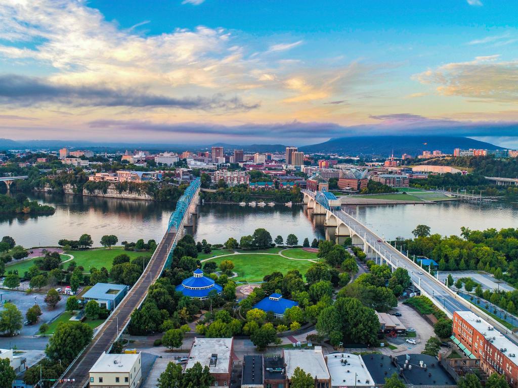 Chattanooga, TN, USA with a drone aerial of the downtown skyline, with Coolidge Park and Market Street Bridge in the foreground on a sunny day just before sunset.
