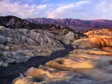 Zabriskie Point at Death Valley National Park with rolling mountains and the sun casting shadows.