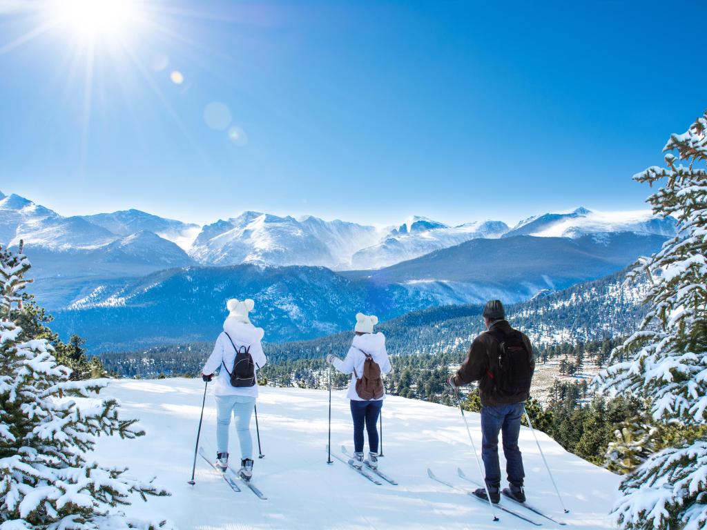 A group of three skiers near Estes Park in Colorado, on top of a snow-covered hill under the blue sky
