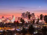 Los Angeles Skyline in the distance at sunset, with palm trees in the foreground, with the moon rising faintly behind