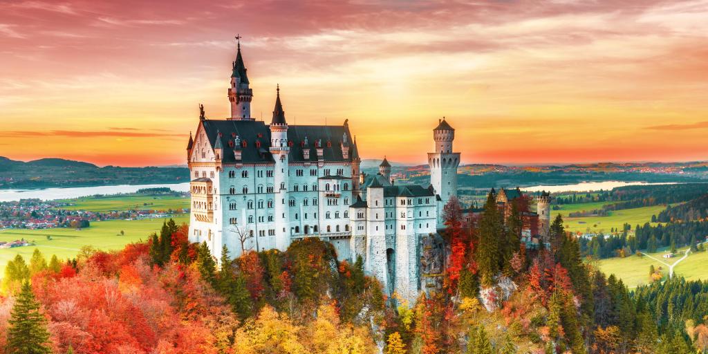 Neuschwanstein castle in Bavaria, Germany, surrounded by yellow and orange autumnal trees, at sunrise