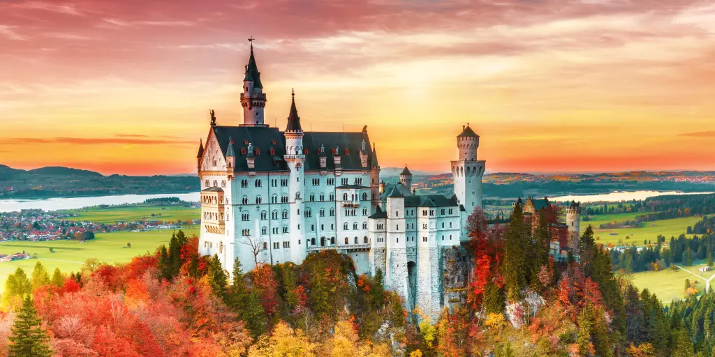 Neuschwanstein castle in Bavaria, Germany, surrounded by yellow and orange autumnal trees, at sunrise