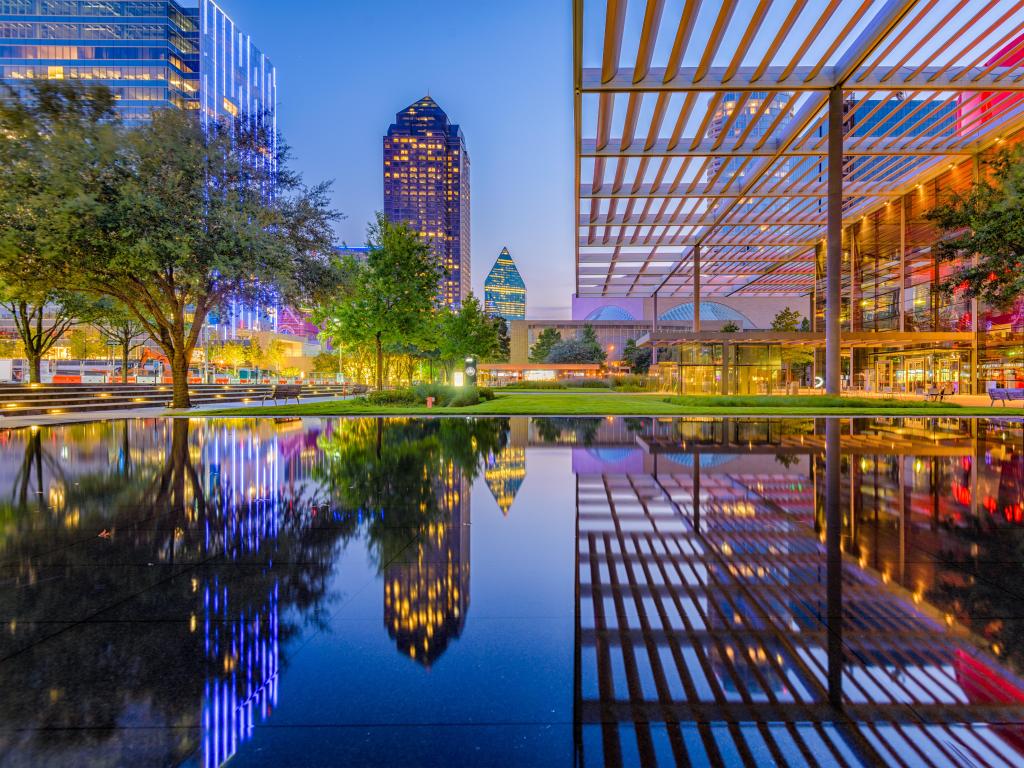 Two tall buildings in the background reflected in still water in the foreground, in deep blue and pink twilight light