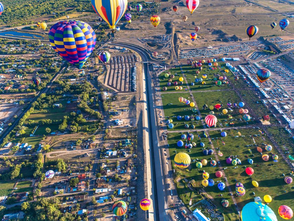 Albuquerque Balloon Fiesta, USA with multiple colorful balloons in the sky looking down on an aerial view of the city on a sunny day.