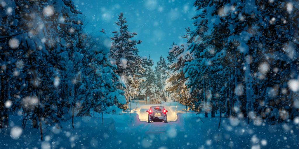 Lights of a car and winter snowy road in a dark forest at night