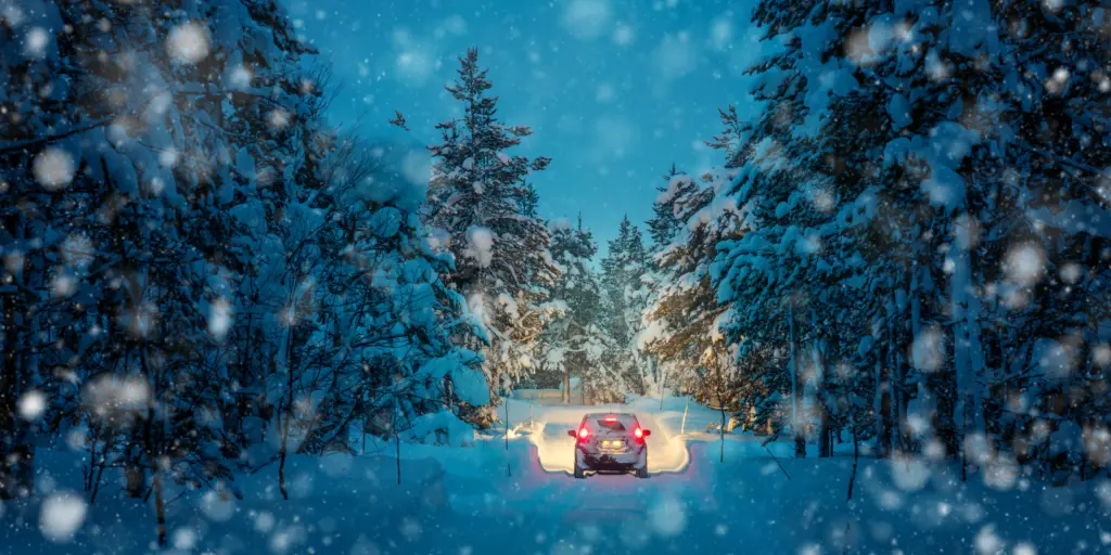 Lights of a car and winter snowy road in a dark forest at night