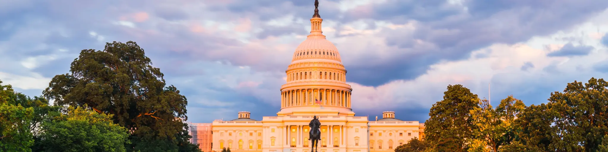 The United States Capitol building below a purple sunset with reflection in water.