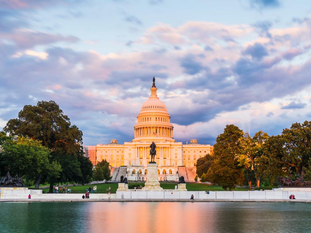 The United States Capitol building below a purple sunset with reflection in water.