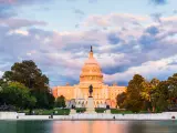 The United States Capitol building below a purple sunset with reflection in water.