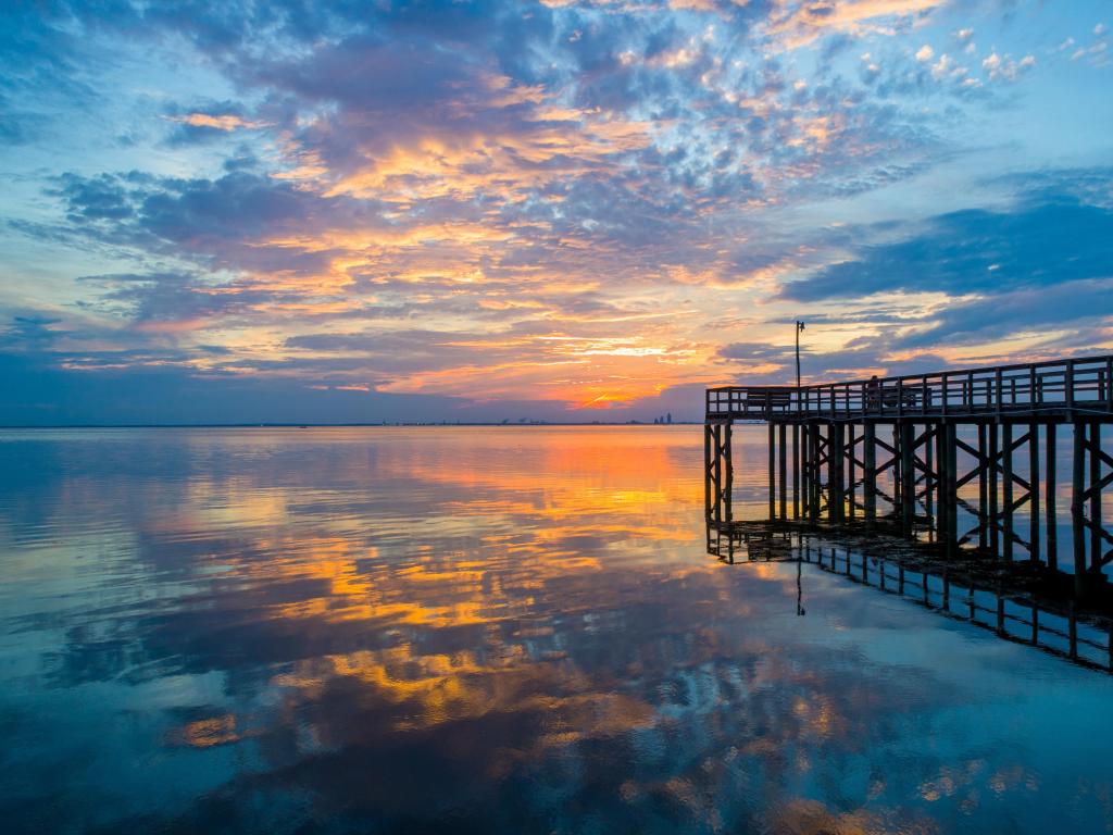 Beautiful colorful sunset reflecting on a calm sea with silhouetted pier over the water