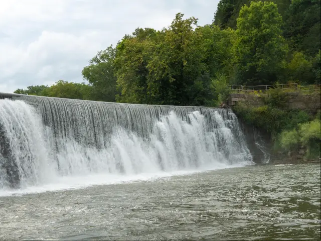 Root River in Lanesboro, Minnesota, USA with mist rising from a Weir waterfall on the Root River on a cloudy day.