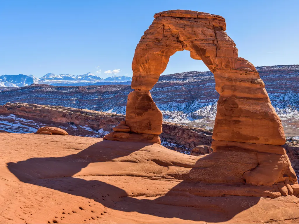 A closeup view of Delicate Arch, with snow-covered La Sal Mountains in background, on a clear sunny winter day. Arches National Park, Utah, USA.