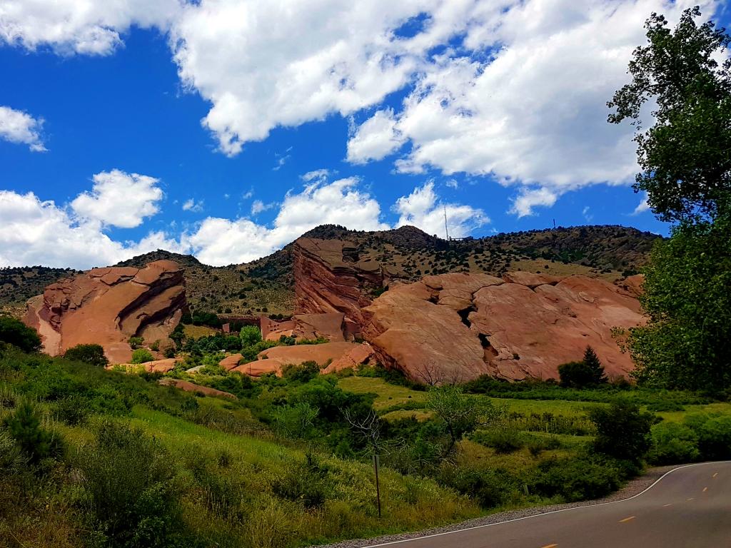A view of Red Rocks Amphitheatre from the road surrounded by trees during daytime.